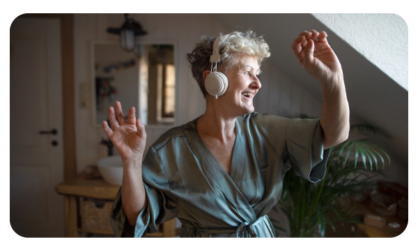 Older woman in a bathrobe and headphones dances in her room